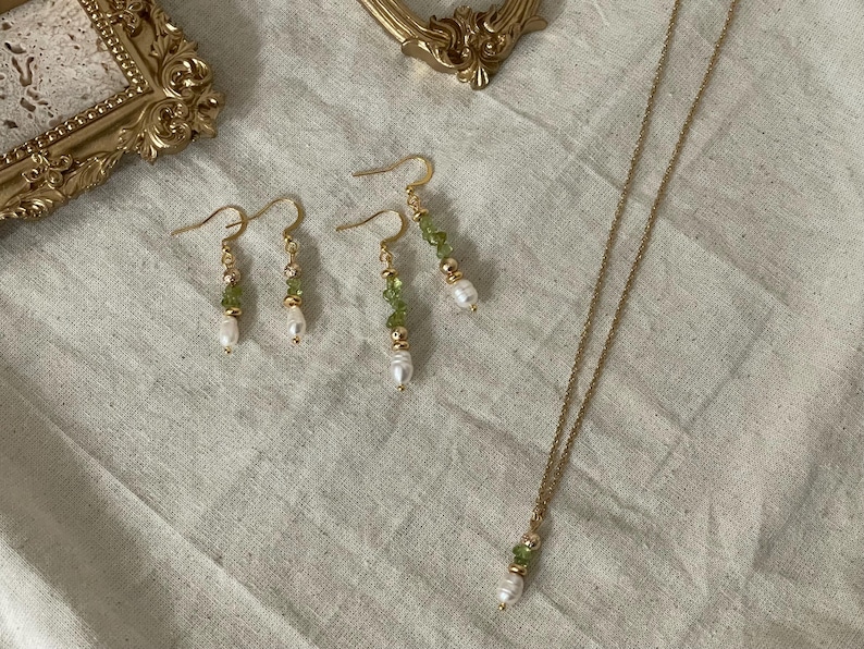 Pu&ograve; includere: Un set di orecchini d'oro e una collana con perline verdi e bianche. Gli orecchini sono orecchini pendenti con una perla in fondo. La collana &egrave; una semplice catena con una perla e perline verdi all'estremit&agrave;.