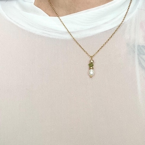 Pu&ograve; includere: Una collana con catena dorata con un piccolo ciondolo di perla e pietra verde.
