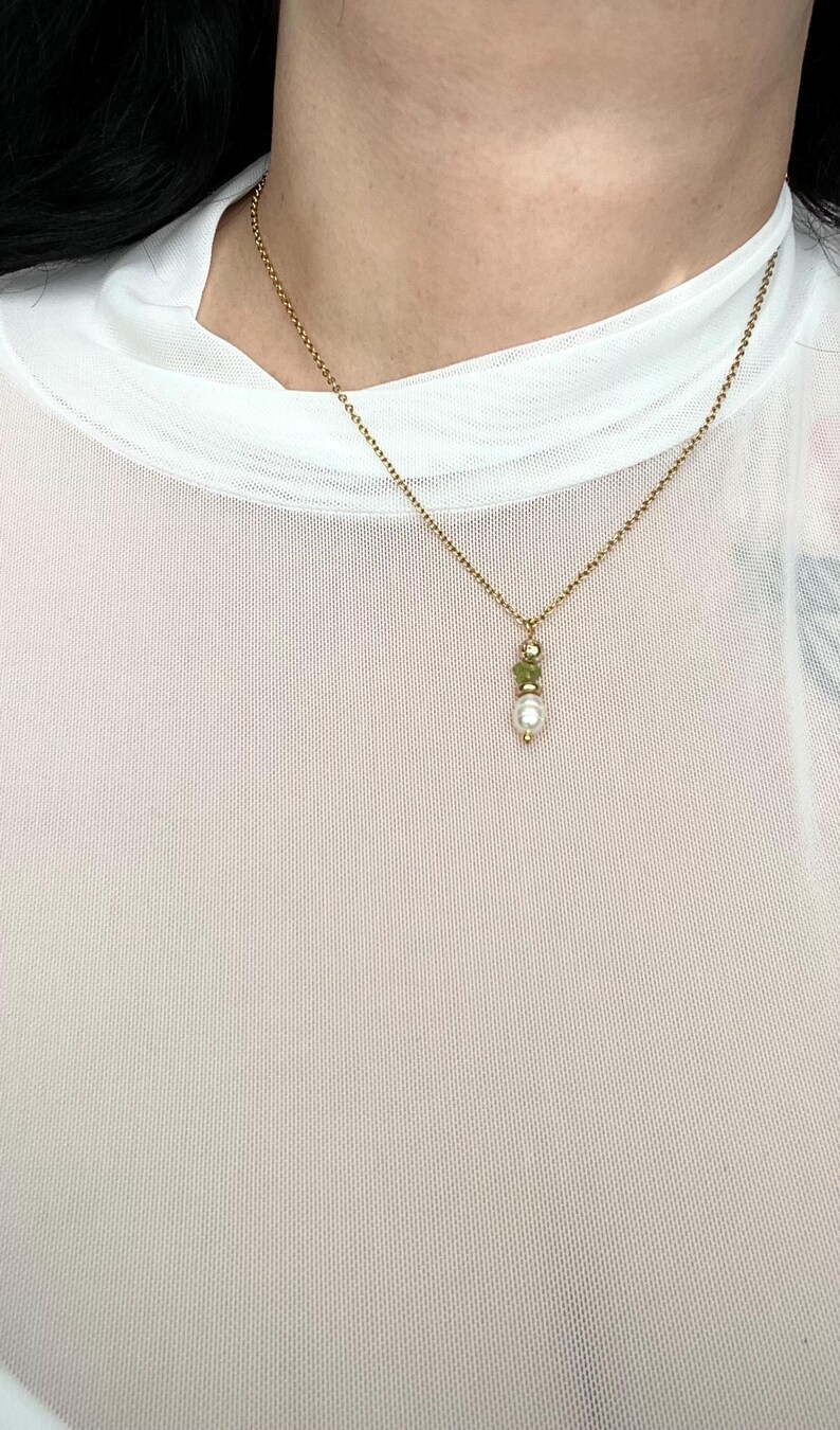 Pu&ograve; includere: Una collana con catena dorata con un piccolo ciondolo di perla e pietra verde.