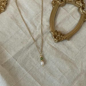 Pu&ograve; includere: Una collana con catena dorata con un ciondolo di perla e pietra preziosa verde.