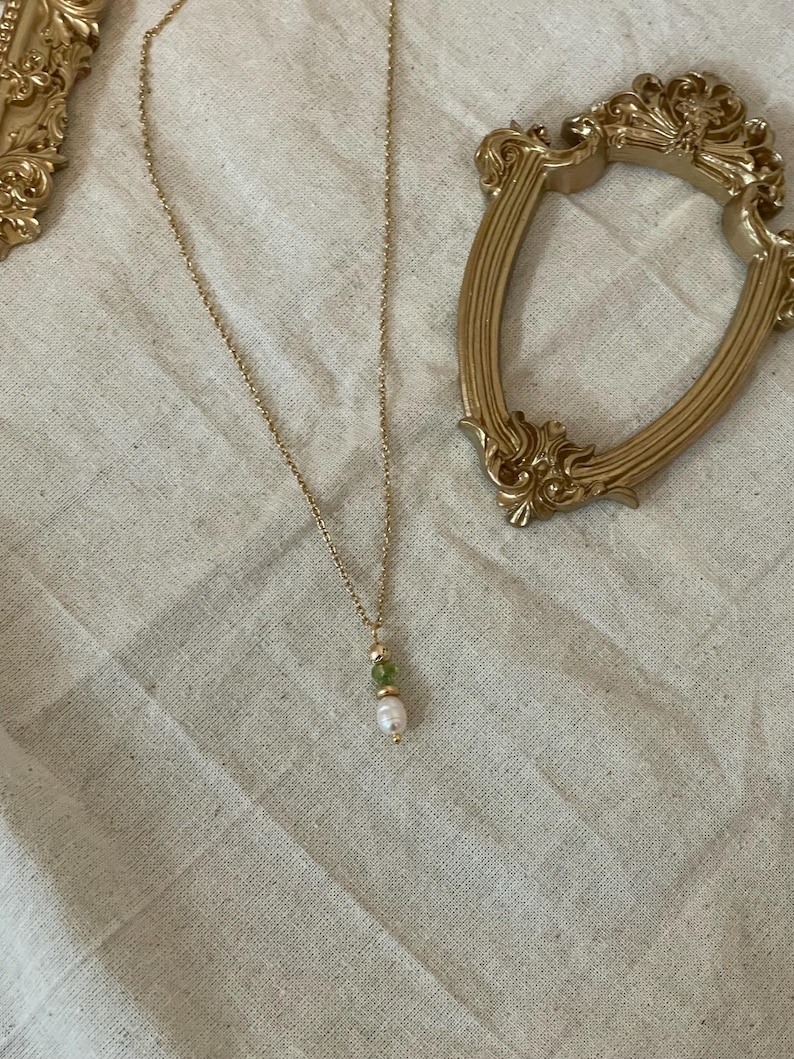 Pu&ograve; includere: Una collana con catena dorata con un ciondolo di perla e pietra preziosa verde.