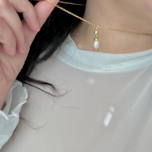 Pu&ograve; includere: Una collana a catena dorata con un piccolo ciondolo di perla e pietra preziosa verde.