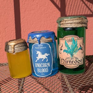 May include: Three decorative glass jars with textured lids. One jar contains yellow liquid, another blue liquid with a label that reads "Unicorn Blood", and the third green liquid with a label that reads "Dirnroot".
