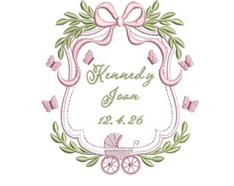 May include: Embroidered design featuring a pink bow, a decorative frame, butterflies, and a baby carriage. The name "Kennedy Joan" and the date "12.4.26" are displayed in elegant script. Green leaves and pink accents complete the design.