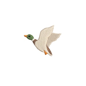 May include: Embroidered patch of a flying duck. The duck has a green head, orange beak and feet, and a beige body and wings. The wings are outstretched, and the duck is in mid-flight against a white background.
