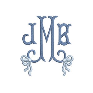Pode incluir: Um monograma bordado em azul claro com as letras J, M e B. As letras são estilizadas com enfeites decorativos e são acompanhadas por dois laços em um tom de azul mais claro, um na parte inferior esquerda e outro na parte inferior direita.
