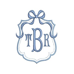 May include: A light blue monogram design featuring the letters TBR within a decorative frame. The frame is adorned with a bow at the top and a scalloped edge. The design is embroidered on a white background.
