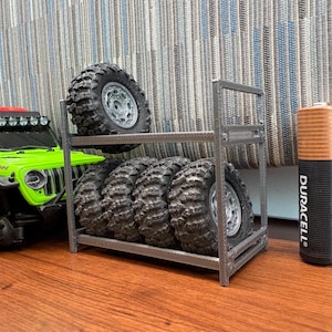 Puede incluir: Un Jeep Wrangler Rubicon de juguete verde lima con un estante negro para neumáticos que contiene cinco neumáticos negros con llantas plateadas. Una gran batería AA Duracell está al lado del estante. La batería está impresa con "MAR 2037".