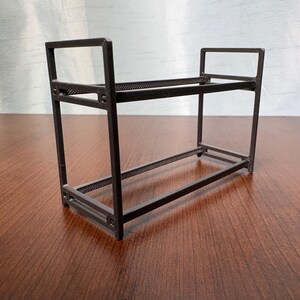 Può includere: Un ripiano rettangolare a due livelli di colore marrone scuro con un design a telaio aperto. La struttura è composta da quattro montanti verticali angolari collegati da barre orizzontali, creando due livelli distinti per l'organizzazione.