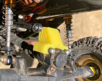 May include: Close-up of a yellow 3D printed part attached to a black metal axle. The part has a textured surface and is designed to fit over the axle. The axle is connected to a black metal gear box.