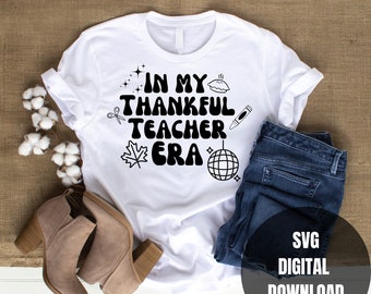 May include: White t-shirt with black text that reads "In My Thankful Teacher Era" with various icons including a pie, scissors, a crayon, a leaf, and a disco ball. The t-shirt is on a brown burlap background with a pair of brown boots and blue jeans.