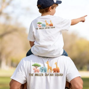 Puede incluir: Dos camisetas blancas con un gráfico de un árbol verde, un elefante rosa, un elefante azul, una jirafa y un oso marrón, con el texto THE MILLER SAFARI SQUAD impreso en marrón debajo de los animales en la parte posterior de cada prenda.