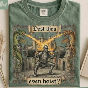 May include: Moss green t-shirt with a medieval graphic. The design shows a knight lifting a barbell, with dragons breathing fire, and the text "Dost thou even hoist?" The shirt has a crew neck and short sleeves.
