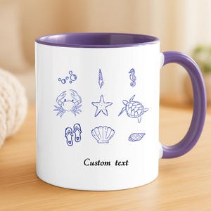 Puede incluir: Taza de cerámica blanca con interior y asa morados. La taza presenta dibujos lineales azules de conchas marinas, un cangrejo, una estrella de mar, un caballito de mar y otros iconos con temática de playa. El texto "Custom text" está impreso debajo.
