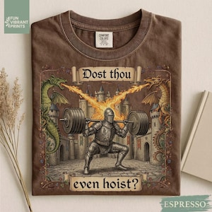 Könnte beinhalten: Espressofarbenes T-Shirt mit mittelalterlichem Motiv. Das Design zeigt einen Ritter, der Gewichte hebt, flankiert von Drachen, mit dem Text "Dost thou even hoist?" Das Shirt hat einen Rundhalsausschnitt und ein Comfort Colors-Etikett.