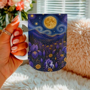 Puede incluir: Una taza de cerámica blanca con un estampado artístico vibrante de un cielo nocturno con una gran luna amarilla, nubes arremolinadas y un campo de lirios morados y pequeñas flores amarillas. El nombre Kelly está escrito en letra blanca.