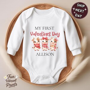 May include: White baby onesie with long sleeves, featuring the text "MY FIRST Valentines Day" in black and red. Below the text are three cartoon cows with Valentine's Day accessories. The name "ALLISON" is printed below the cows.