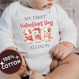 May include: White baby onesie with long sleeves. The onesie features the text "MY FIRST Valentines Day" above an illustration of three cartoon cows. The name "ALLISON" is printed below the cows. A circular graphic reads "100% COTTON".
