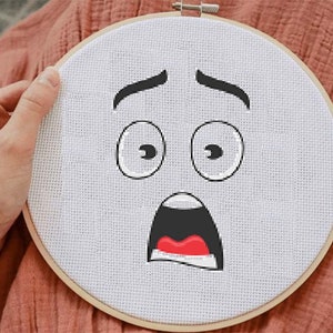 May include: A white embroidery hoop with a hand-stitched cartoon face with wide eyes and an open mouth, expressing surprise or fear.