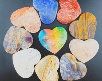 Op de afbeelding: Een verzameling van tien hartvormige stenen in diverse kleuren en patronen, waaronder blauw, rood, oranje, geel, wit en paars, gerangschikt in een cirkel. Elke steen vertoont unieke natuurlijke texturen, minerale aders en kleurverlopen.