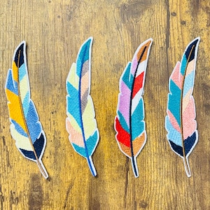 May include: Five colorful embroidered iron-on patches in the shape of feathers. The feathers are in shades of blue, yellow, red, pink, and white.