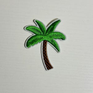May include: Embroidered palm tree patch featuring a green frond and a brown trunk. The patch has a white border. This tropical-themed patch can be ironed on or sewn onto clothing or accessories.