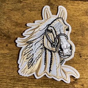 May include: White embroidered horse head patch with a black bridle. The horse has a flowing mane and a detailed face.