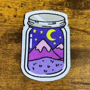 May include: A patch featuring a jar with a night scene. Inside the jar are purple mountains, a crescent moon, and stars against a dark blue background. The jar has a silver lid and a white border.