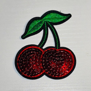 May include: A red and green cherry patch with sequins. The cherries are sewn together with a green stem and leaves.