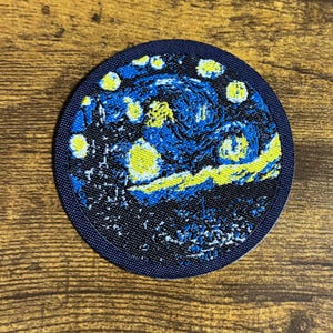 May include: Round patch featuring a detailed embroidered depiction of Van Gogh's "Starry Night" painting. The design showcases swirling blues, yellows, and whites, with a dark blue border. The patch is likely for clothing or accessories.