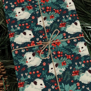 May include: A gift wrapped in blue wrapping paper with a pattern of white opossums, red berries, and green leaves. The paper is tied with twine.
