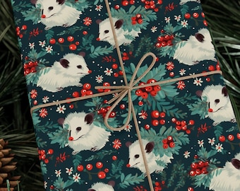 Könnte beinhalten: Ein Geschenk, das in blaues Geschenkpapier mit einem Muster aus weißen Opossums, roten Beeren und grünen Blättern eingewickelt ist. Das Papier ist mit Schnur gebunden.