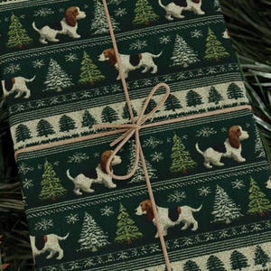 May include: A wrapped gift with a green background featuring a repeating pattern of white and brown dogs, Christmas trees, and snowflakes. The gift is tied with a light brown string.
