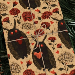 Puede incluir: Paquete de regalo con un patrón repetido de criaturas negras parecidas a polillas con corazones y ojos rojos, flores rojas y blancas y pequeños corazones rojos sobre un fondo beige. Atado con una cuerda gris plateada.
