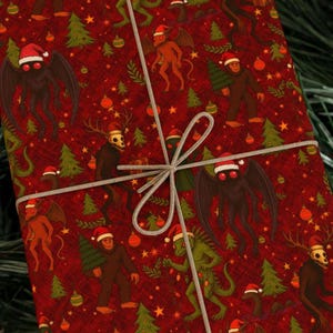 May include: A wrapped gift with a red background featuring various cryptids wearing Santa hats, Christmas trees, and ornaments. The gift is tied with a gray string and bow. The cryptids include Mothman, Bigfoot, and other mythical creatures.