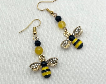 Può includere: Un paio di orecchini a forma di ape dorati con smalto giallo e nero e strass trasparenti. Ogni orecchino ha una perla nera e una perla gialla.