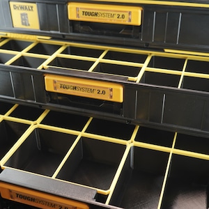 May include: Close-up of a black and yellow tool box with two drawers. The drawers are divided into multiple compartments. The drawers are labelled "TOUGHSYSTEM 2.0".