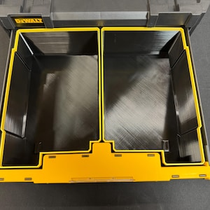 May include: Black and yellow DeWalt tool organiser with two compartments. The organiser has a yellow frame and a black interior. The DeWalt logo is visible on the top left corner. Designed for storing tools and accessories.