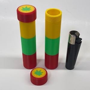 May include: Two cylindrical containers with red, yellow and green stripes and a green leaf design on the lids. One lid is off and sitting next to the containers. A black lighter is next to the containers.