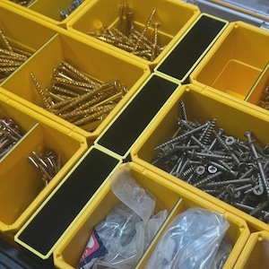 May include: A yellow organiser filled with various types of screws. The screws are in different sizes and finishes, including gold and silver. The organiser has black dividers separating the compartments.