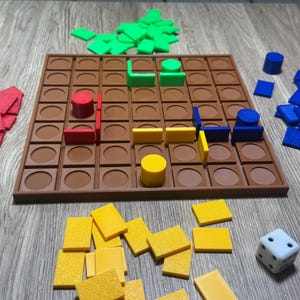 May include: A brown board game with a grid pattern, surrounded by various game pieces. The pieces are in red, green, yellow, and blue, including cylinders, rectangles, and a die. The game is set on a wooden surface.