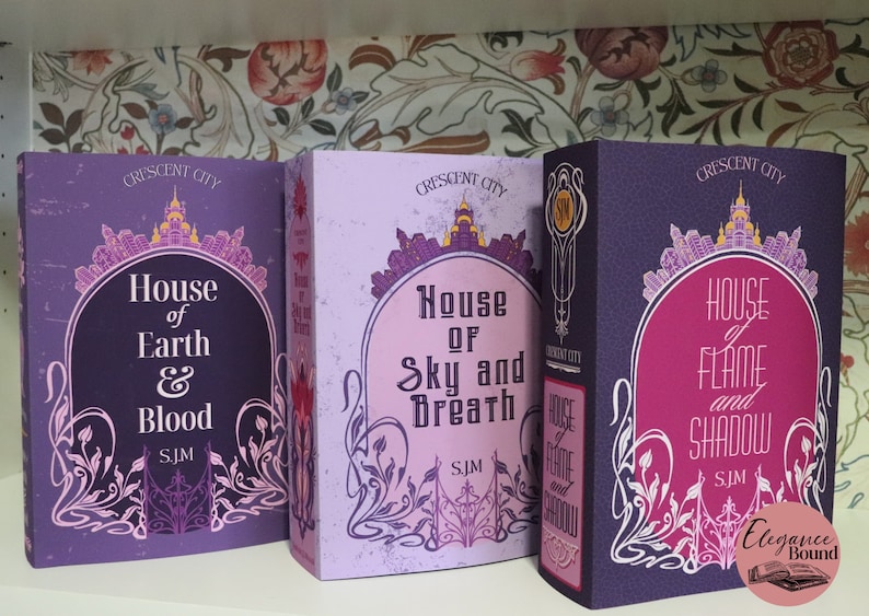 May include: Three hardcover books from the "Crescent City" series, featuring titles "House of Earth & Blood", "House of Sky and Breath", and "House of Flame and Shadow". Each book has a unique color scheme with ornate designs and text.
