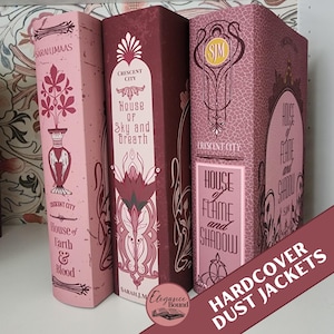 Puede incluir: Tres sobrecubiertas de libros de tapa dura en tonos rosa y burdeos. Las lomos presentan diseños ornamentados y títulos como "House of Earth & Blood", "House of Sky and Breath" y "House of Flame and Shadow". El texto "HARDCOVER DUST JACKETS" también es visible.