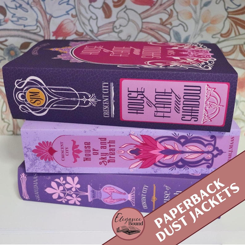 May include: Three paperback dust jackets stacked on top of each other. The top jacket is dark purple with pink text that reads "House of Flame and Shadow". The middle jacket is light purple with pink floral designs. The bottom jacket is purple with pink floral designs.