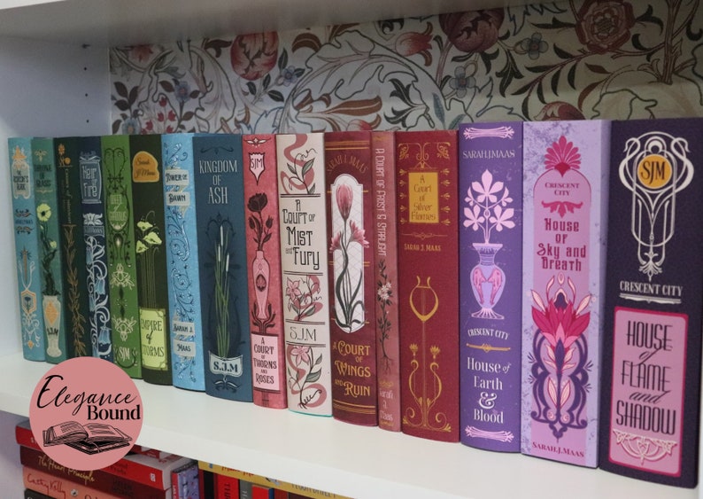 May include: A collection of fantasy novels with decorative covers, arranged on a white shelf. The books feature various colors, including blue, green, red, and purple, with floral and geometric designs. The text "Elegance Bound" is in a pink circle.