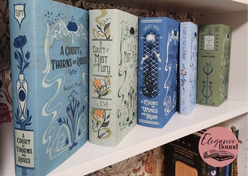 May include: A collection of fantasy novels with decorative covers. The books are in various shades of blue, green, and white, with floral and abstract designs. Titles include "A Court of Thorns and Roses" and "A Court of Mist and Fury."