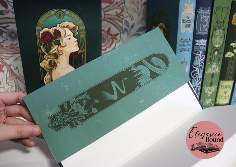 Pode incluir: Um di&aacute;rio azul-petr&oacute;leo com um design art nouveau apresentando uma mulher com rosas e uma borda decorativa. O di&aacute;rio aberto revela p&aacute;ginas brancas. Outros livros com capas decorativas s&atilde;o vis&iacute;veis ao fundo.