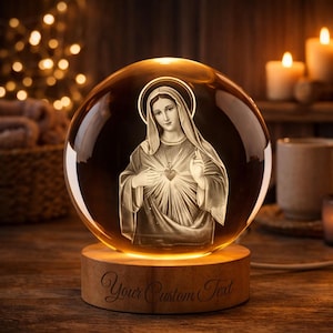 May include: A glowing glass sphere with an engraved image of a religious figure, set on a wooden base. The sphere is lit from within, and the base has the text "Your Custom Text". The background includes candles and soft lighting.