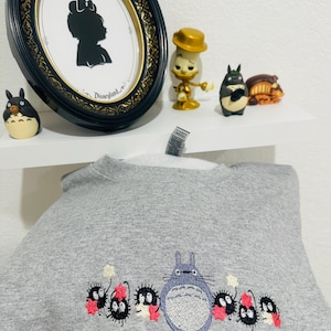 Op de afbeelding: Grijs sweatshirt met een geborduurd beeld van Totoro en de roetgeesten uit de film Mijn buurman Totoro. De roetgeesten houden sterren vast en staan voor Totoro.