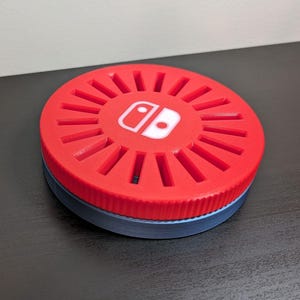 May include: A red and blue circular game cartridge storage case with a Nintendo Switch logo on the top. The case has slots for multiple cartridges.